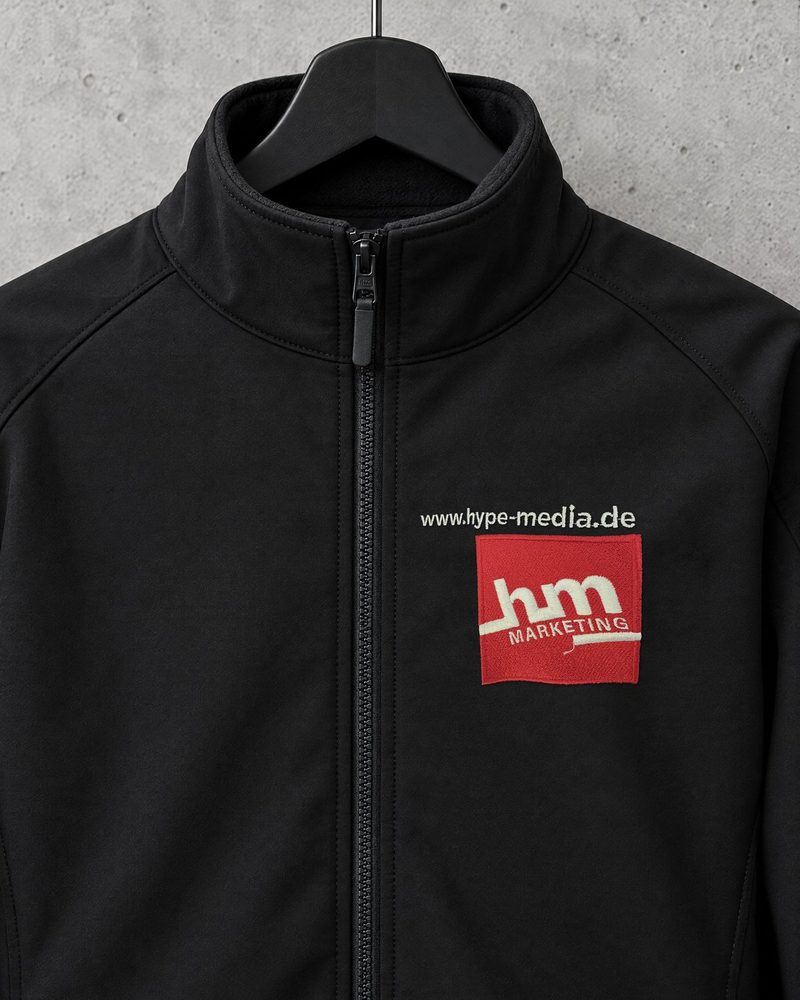 Schwarze Softshelljacke mit rot-weiß gesticktem hype.media-Marketing-Emblem und Schriftzug www.hype-media.de