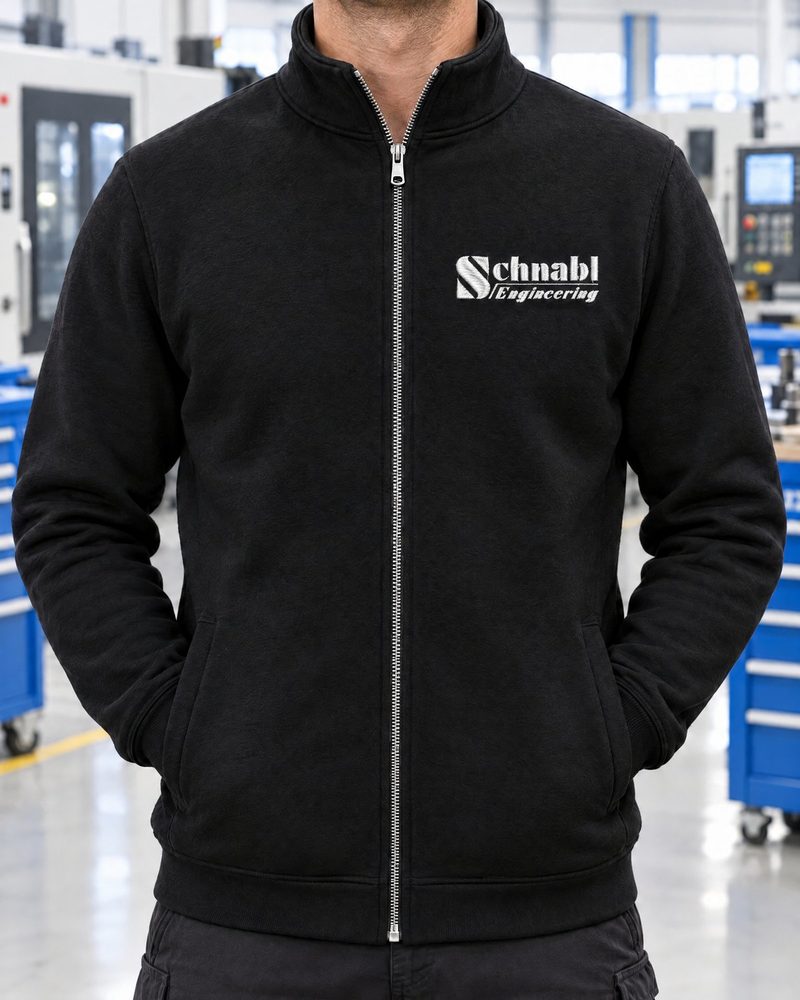 Schwarze Sweatjacke mit weiß gesticktem Schnabl-Engineering-Logo in einer Werkhalle
