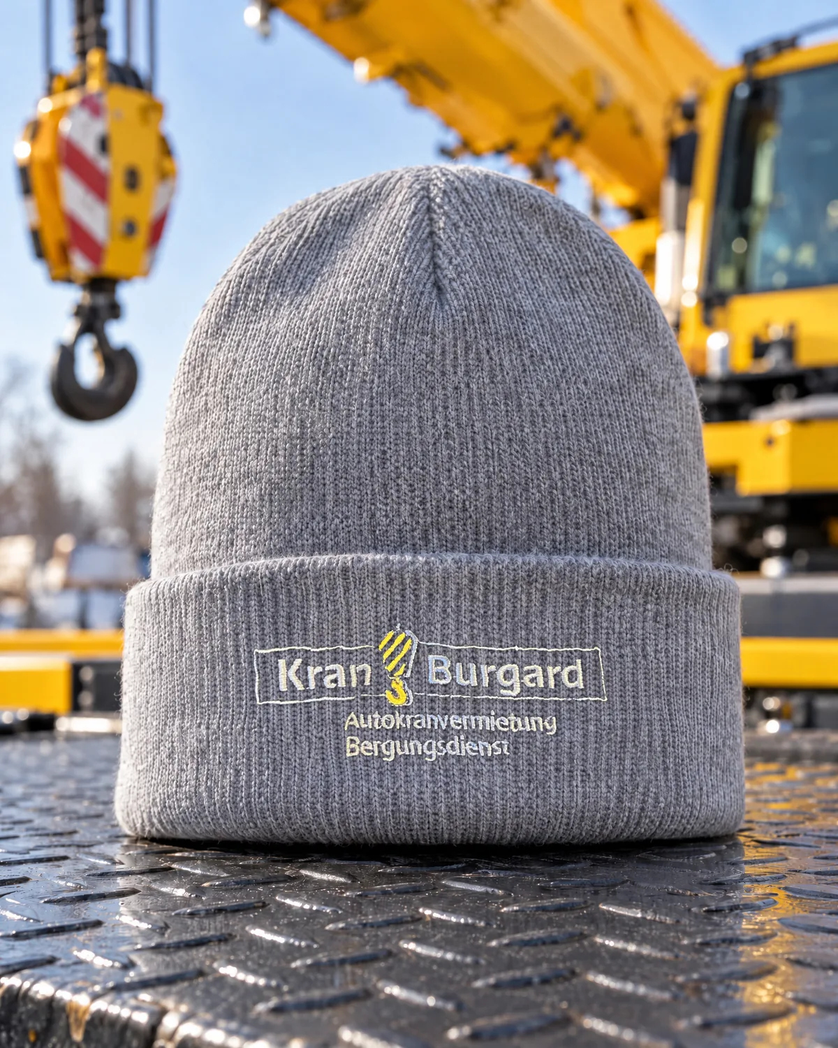 Graue Strickmütze mit gesticktem Kran-Burgard-Logo vor einem Mobilkran