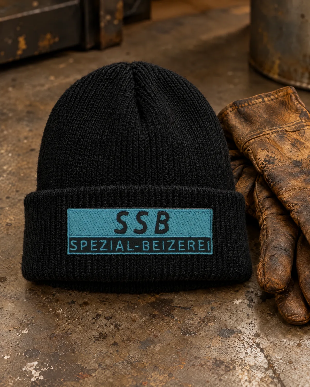 Schwarze Strickmütze mit türkis gesticktem SSB-Spezial-Beizerei-Logo auf dem Umschlag