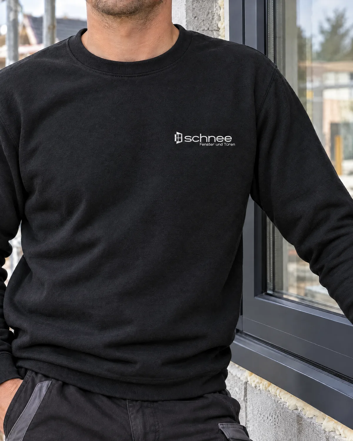 Monteur im schwarzen Sweatshirt mit gesticktem Logo Schnee Fenster und Türen an einem neuen Fenster